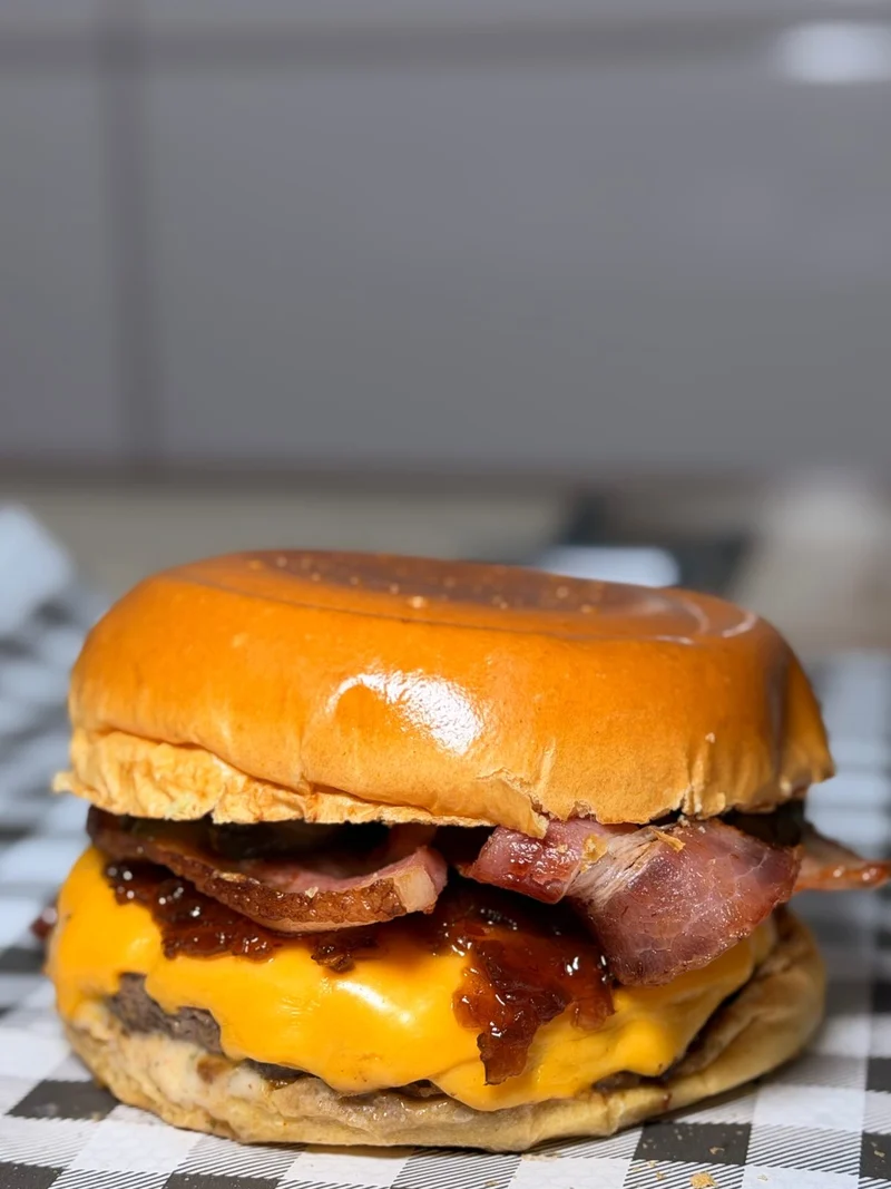 Hambúrguer com cheddar e tiras de bacon sobre papel xadrez